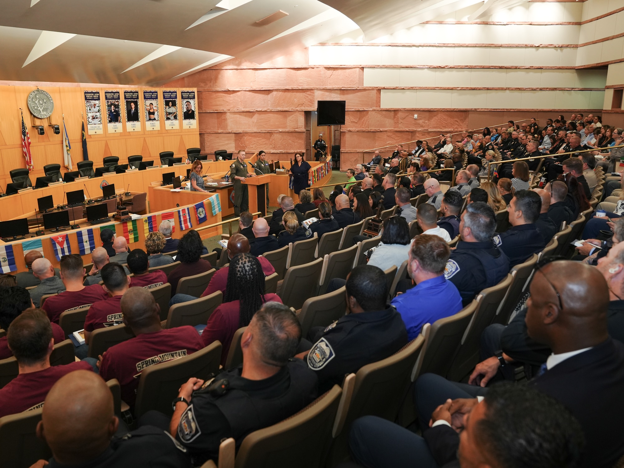A room full of people watch a man in a military uniform give a speech at a podium.