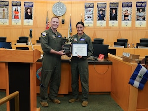 A man and woman in military flight suits smile and hold up an award.