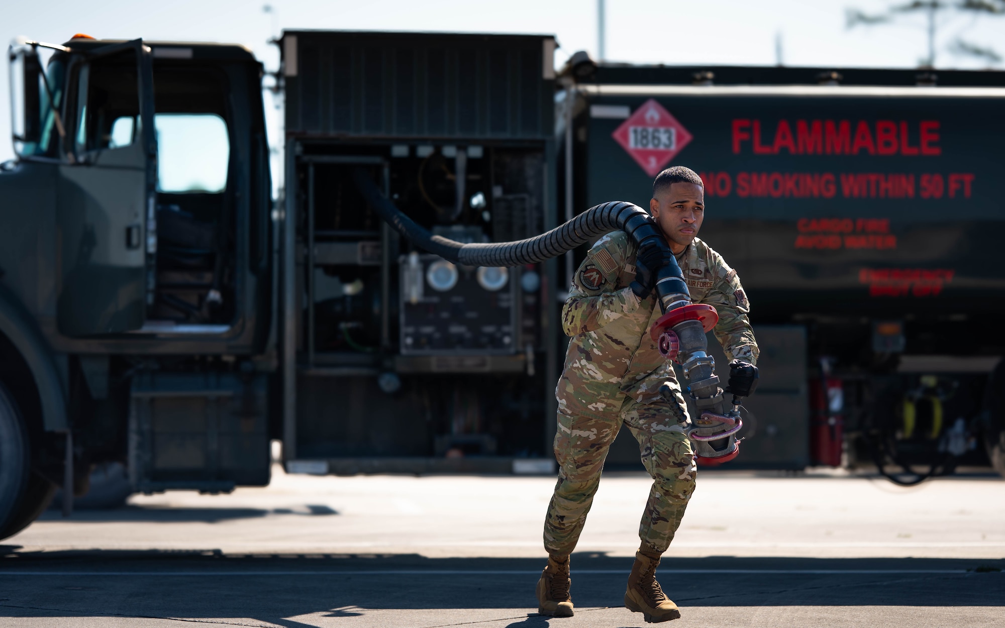 An airman pulls a hose from a fuel truck.