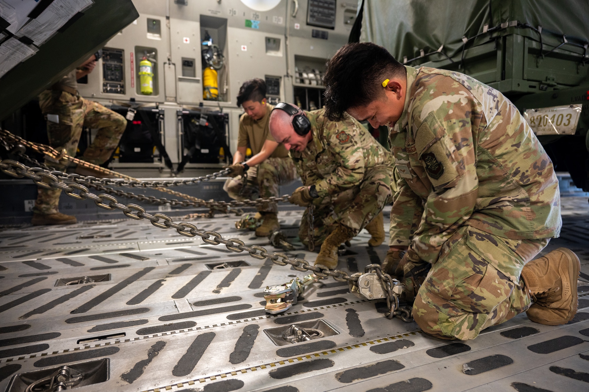 Service members tighten a chain inside an aircraft.