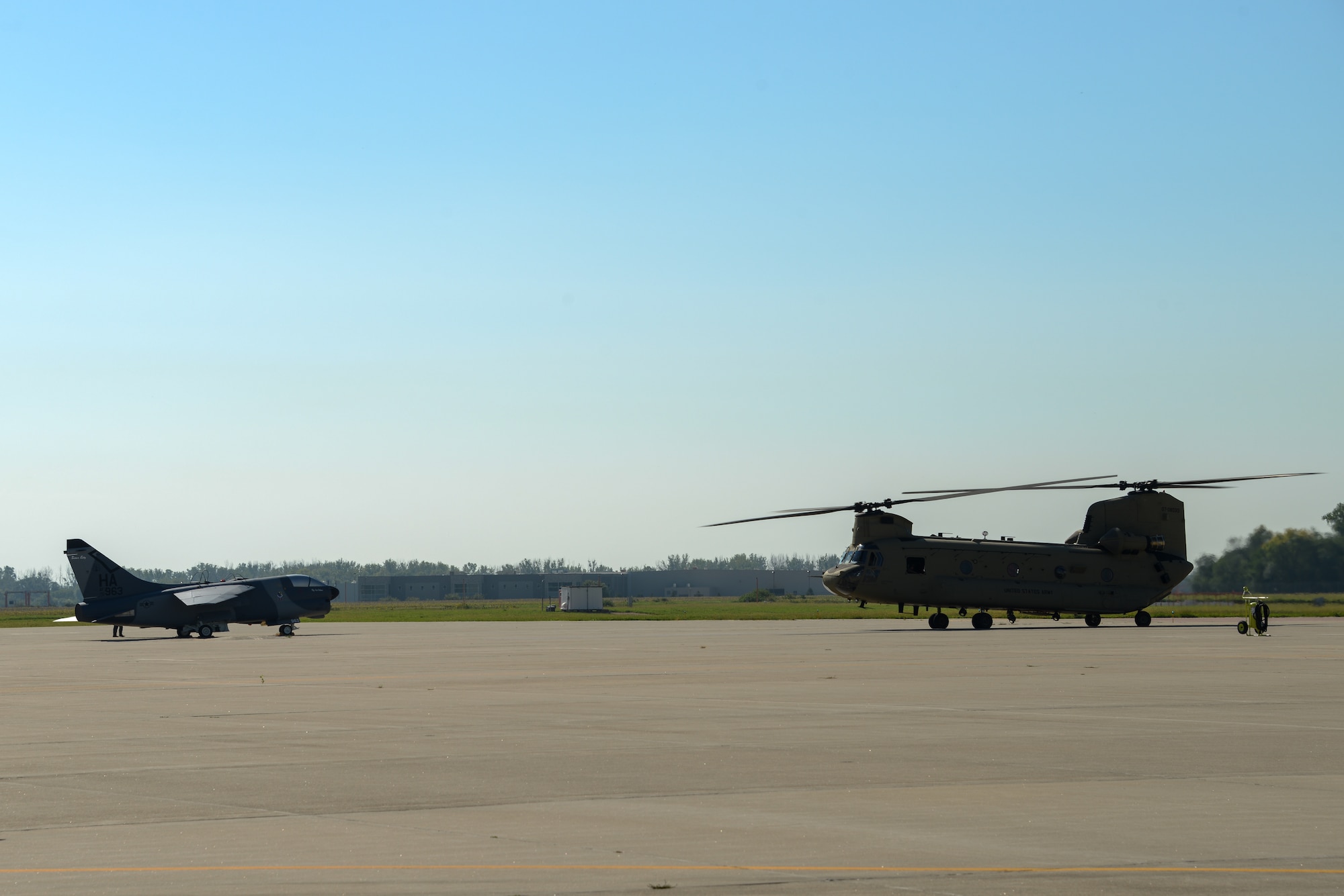 A U.S. Air Force A-7D Corsair II fighter jet static display and a U.S. Army CH-47 Chinook helicopter are parked on a flightline.