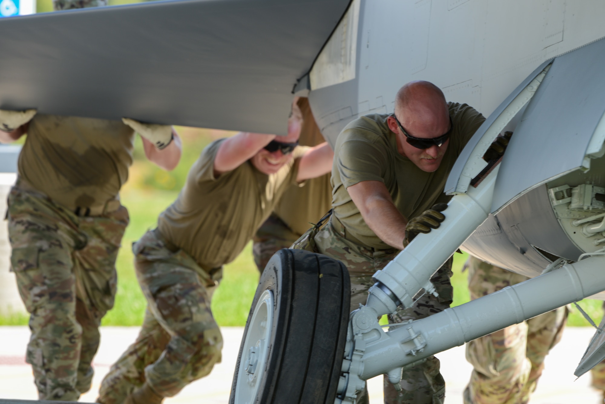 Service members and Air National Guard Paint Facility members push a U.S. Air Force A-7D Corsair II fighter jet static display across mud.