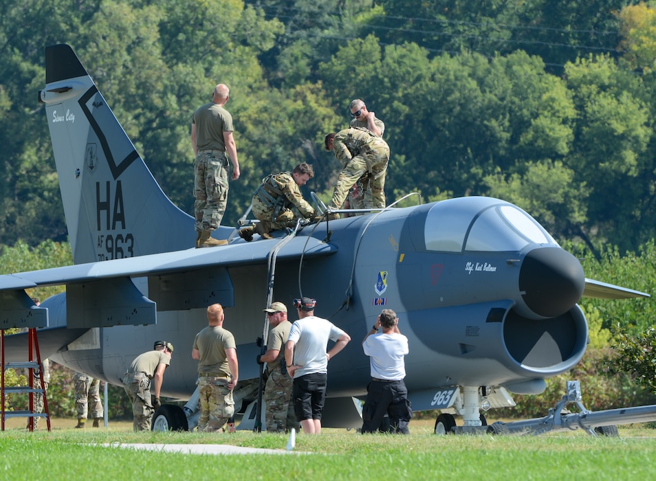 Service members stand atop the wings of a U.S. Air Force A-7D Corsair II fighter jet to remove sling load gear as other service members and Air National Guard Paint Facility members assist from the ground.