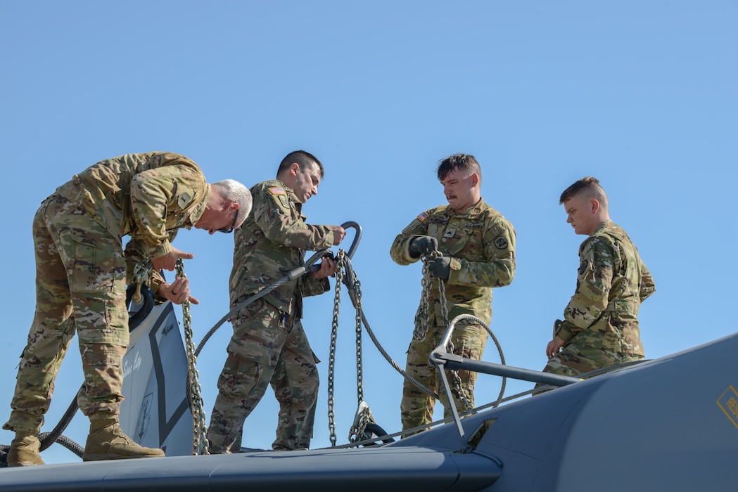Soldiers of Bravo Company, 1st Battalion, 171st Aviation Regiment, stand atop the wings of a U.S. Air Force A-7D Corsair II fighter jet to rig it with sling load gear.