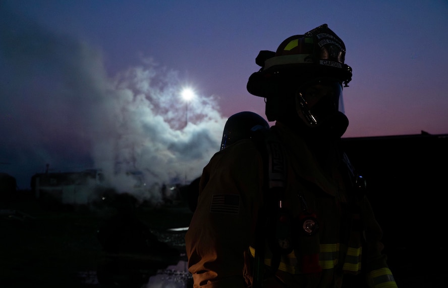 A 5th Civil Engineer Squadron fire protection specialist walks away from an extinguished aircraft fire training facility during a live fire exercise at Minot Air Force Base, North Dakota, Sept. 16, 2025. These military firefighters protect the environment, people and property against fires and disasters. (U.S. Air Force photo by Senior Airman Alyssa Bankston)