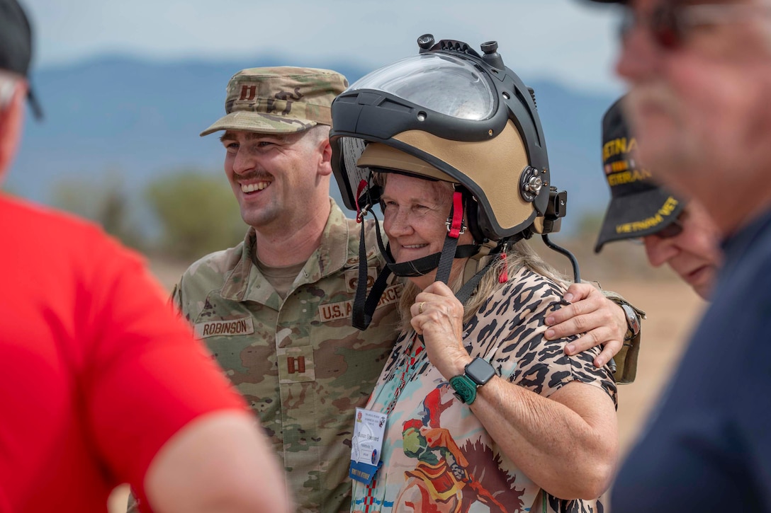 An airman poses with a civilian wearing a helmet as fellow civilians stand nearby.