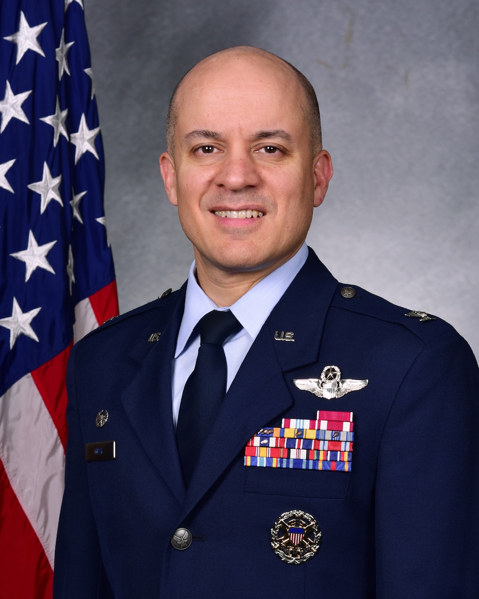 Man poses in front of flag in uniform