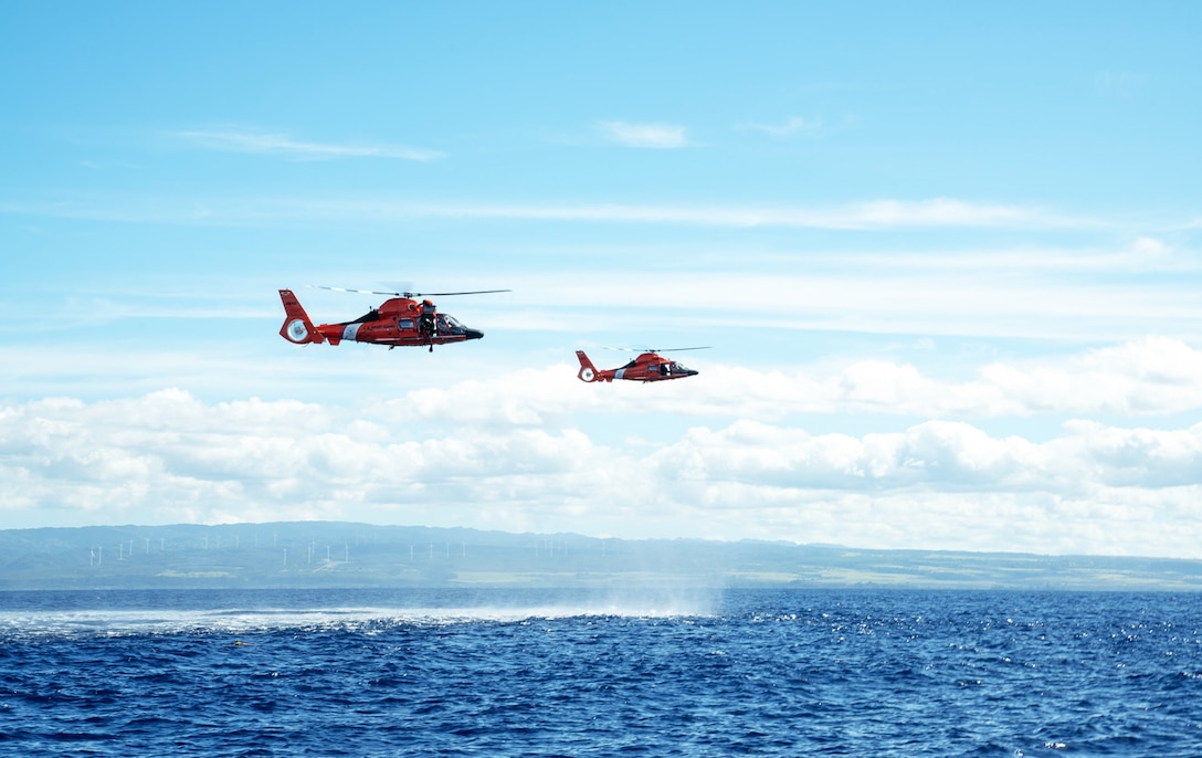 Two Coast Guard MH-65 Dolphin helicopter crews assigned to Coast Guard Air Station Barbers Point, hover over the water while conducting training.