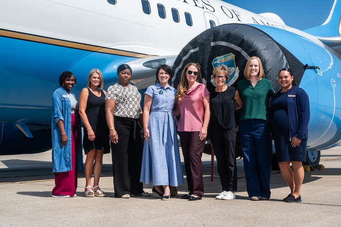 Women pose for a group picture in front of plane