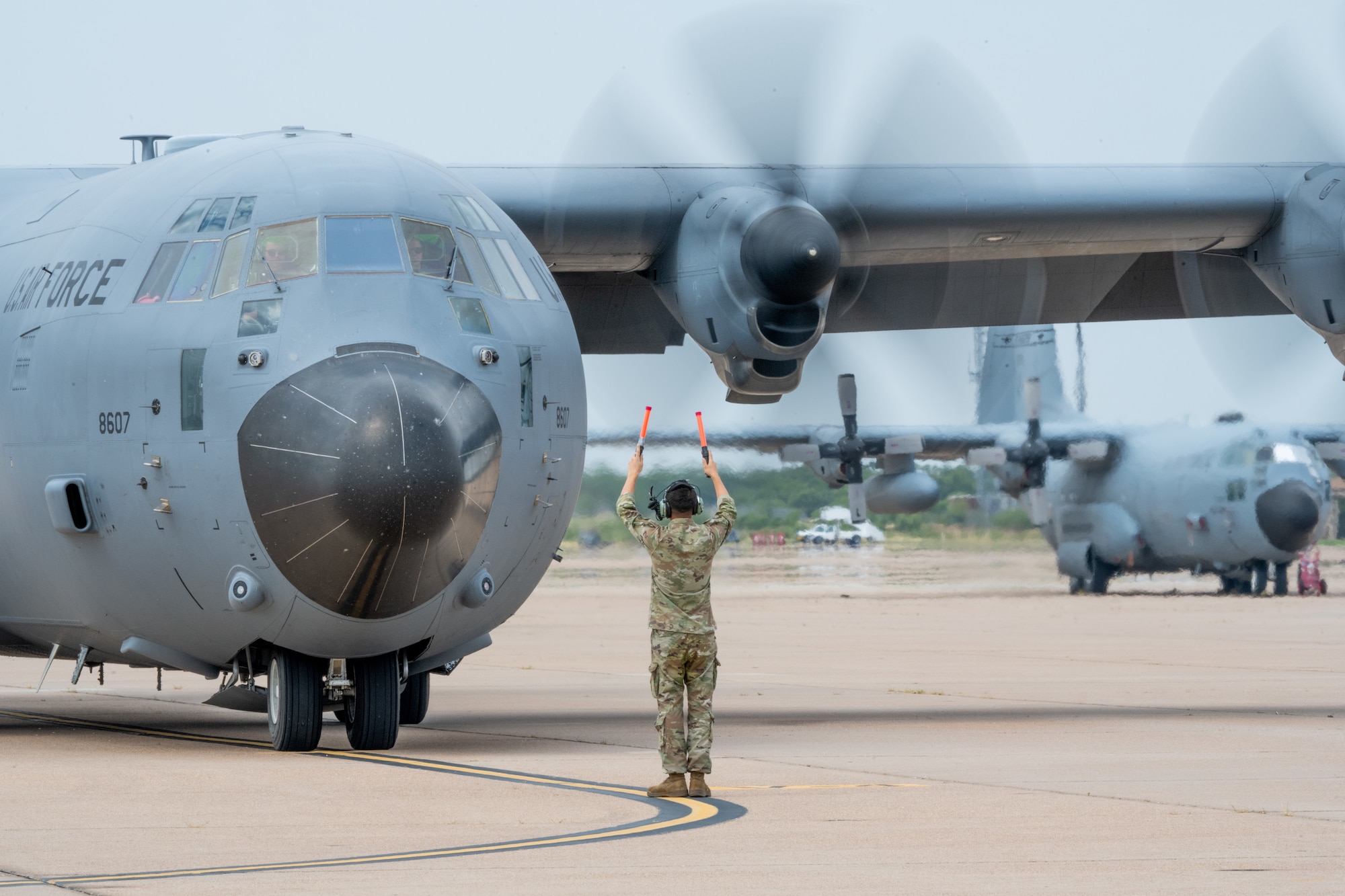 U.S. Air Force Airman assigned to the 317th Airlift Wing, marshals a C-130J Super Hercules to its parking spot on the flightline at Dyess Air Force Base, Texas, Aug. 26, 2025.  During the local training sortie, aircrews conducted low-level flying, airdrops, specialized fueling operations and formation maneuvers to maintain proficiency in a variety of capabilities. (U.S. Air Force Photo by Airman 1st Class Caleb Schellenberg)