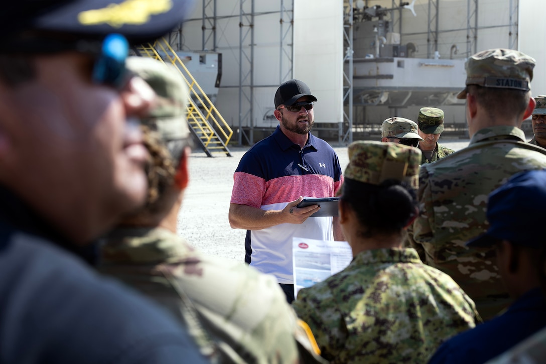 Kevin McCandlish, a Navy equipment specialist with Blount Island Command, explains the Improved Navy Lighterage System—a modular causeway system that resembles a floating pier and is used to transfer cargo—during a tour Sept. 19, 2025, at Marine Corps Support Facility Blount Island in Florida. The overview was given to students visiting from the Western Hemisphere Institute for Security Cooperation. (U.S. Marine Corps photo by Dustin Senger)
