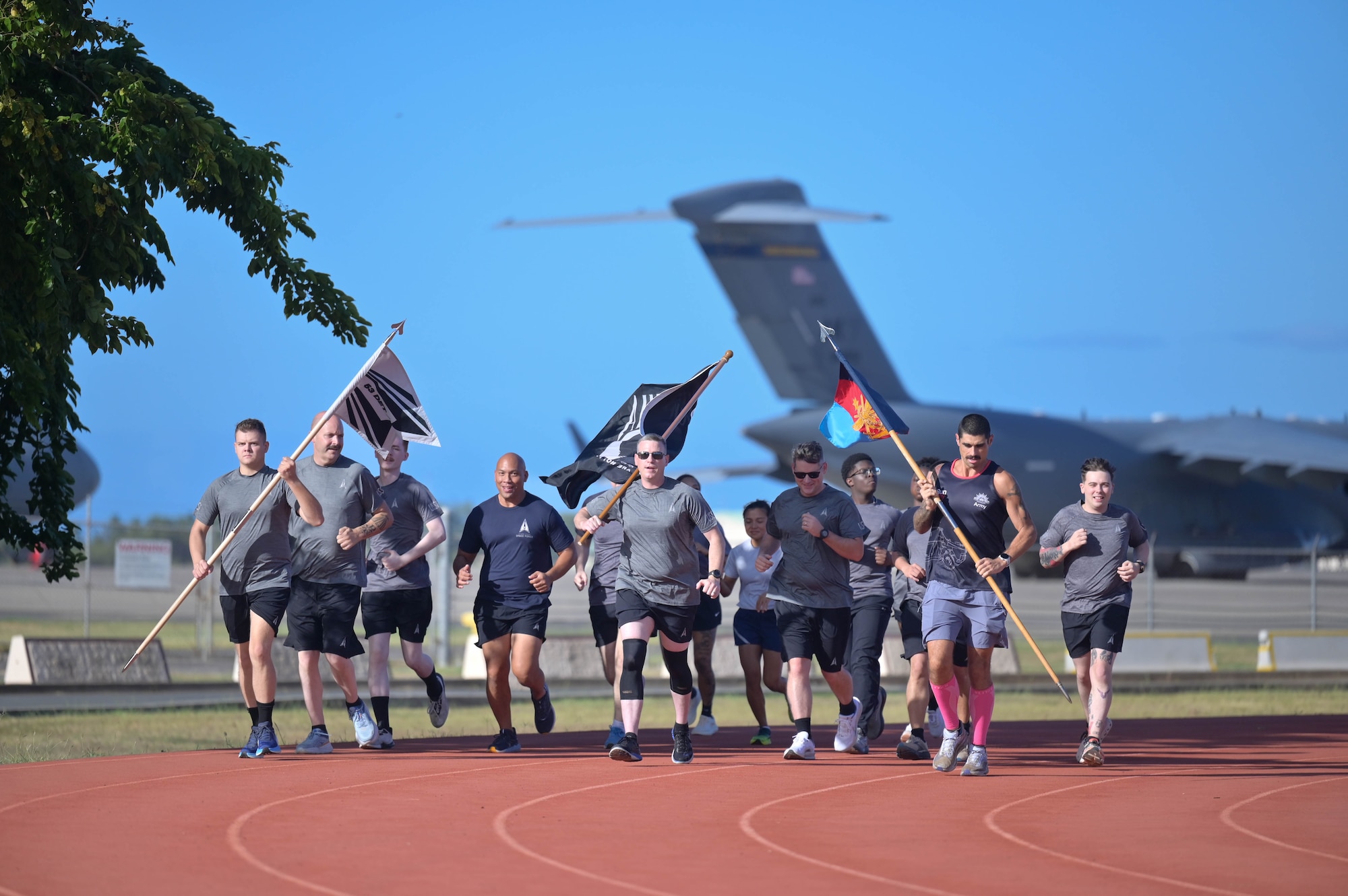 Participants carrying a POW/MIA flag while running on a track with a plane in the background.