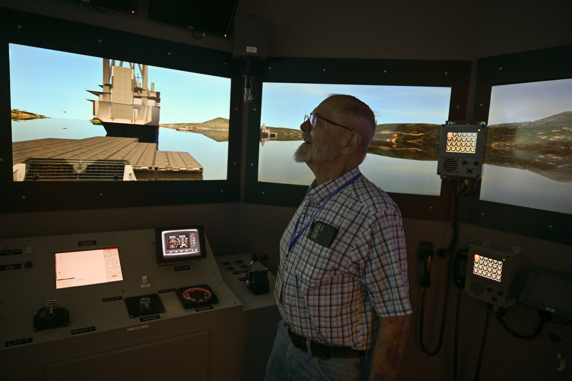 A man stands in a dark room looking at screens that simulate being on a boat and looking through the windows.