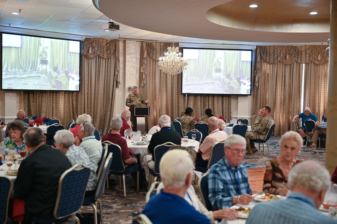 An Army Col. Stands behind a lectern and speaks to people in a fancy dining room.
