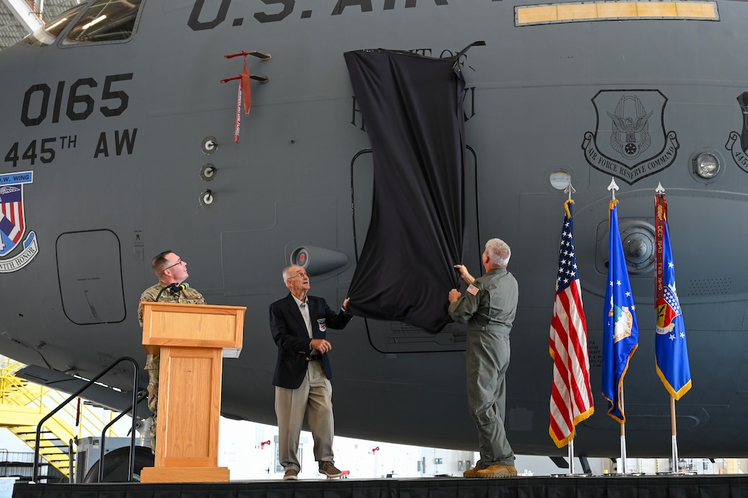 U.S. Air Force Reserve Col. Douglas A. Perry Jr., right, 445th Airlift Wing commander, and retired Maj. Gen. Edward Mechenbier, left, Vietnam veteran and guest speaker, unveil the newly re-designated name of the C-17 Globemaster III with tail number 99-0165 at Wright-Patterson Air Force Base, Ohio, Sept. 19, 2025. The ceremony was part of Operation Honor, paying tribute to the bond between the 445th Airlift Wing and the original C-141 Starlifter Hanoi Taxi, which repatriated American POWs from Vietnam and brought them back home. (U.S. Air Force photo by Staff Sgt. Johnathan Quiñones)
