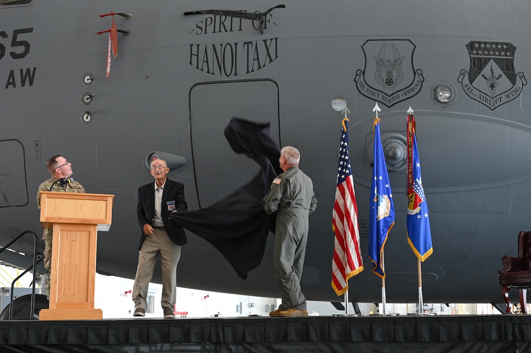 U.S. Air Force Reserve Col. Douglas A. Perry Jr., right, 445th Airlift Wing commander, and retired Maj. Gen. Edward Mechenbier, left, Vietnam veteran and guest speaker, unveil the newly re-designated name of the C-17 Globemaster III with tail number 99-0165 at Wright-Patterson Air Force Base, Ohio, Sept. 19, 2025. The ceremony was part of Operation Honor, paying tribute to the bond between the 445th Airlift Wing and the original C-141 Starlifter Hanoi Taxi, which repatriated American POWs from Vietnam and brought them back home. (U.S. Air Force photo by Staff Sgt. Johnathan Quiñones)