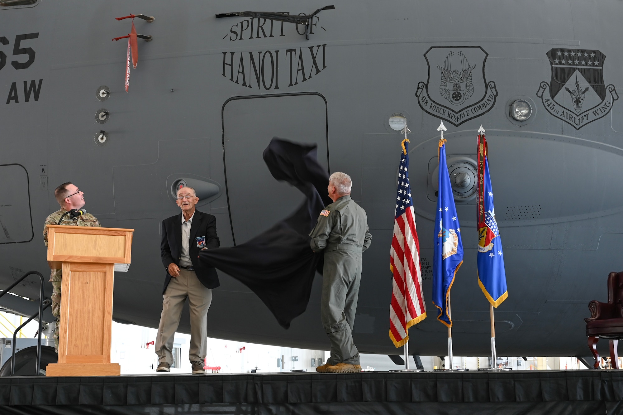 U.S. Air Force Reserve Col. Douglas A. Perry Jr., right, 445th Airlift Wing commander, and retired Maj. Gen. Edward Mechenbier, left, Vietnam veteran and guest speaker, unveil the newly re-designated name of the C-17 Globemaster III with tail number 99-0165 at Wright-Patterson Air Force Base, Ohio, Sept. 19, 2025. The ceremony was part of Operation Honor, paying tribute to the bond between the 445th Airlift Wing and the original C-141 Starlifter Hanoi Taxi, which repatriated American POWs from Vietnam and brought them back home. (U.S. Air Force photo by Staff Sgt. Johnathan Quiñones)