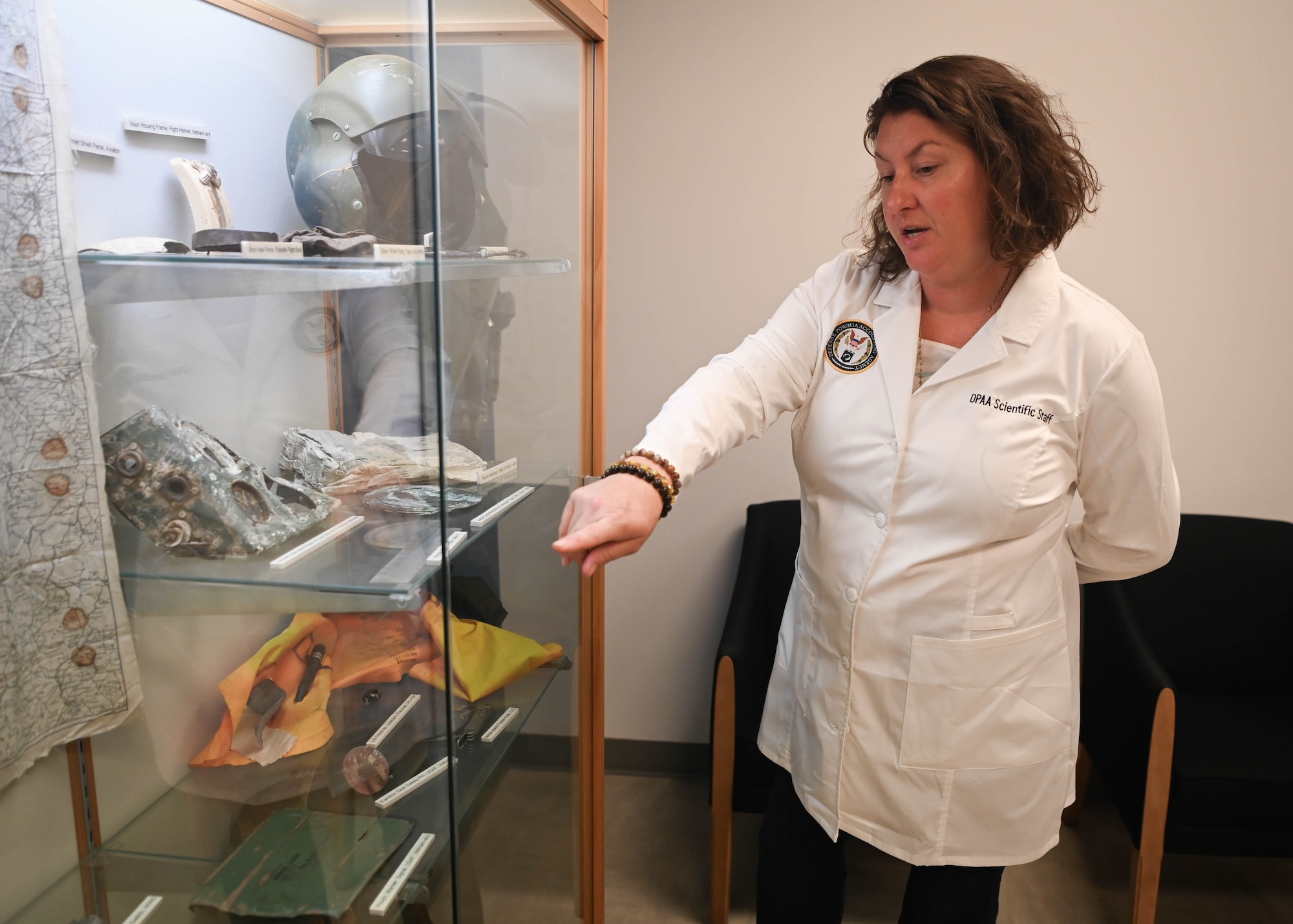 Dr. Carrie Brown, Defense POW/MIA Accounting Agency laboratory manager, points to items from different conflict eras on display at the DPAA facility on Offutt Air Force Base, Neb., Sept. 16, 2025. Military relics, such as those on display, could possibly be found at excavation sites where unidentified remains are recovered, which then are used as material evidence to help in the identification process. (U.S. Air Force photo by Daniel Martinez)