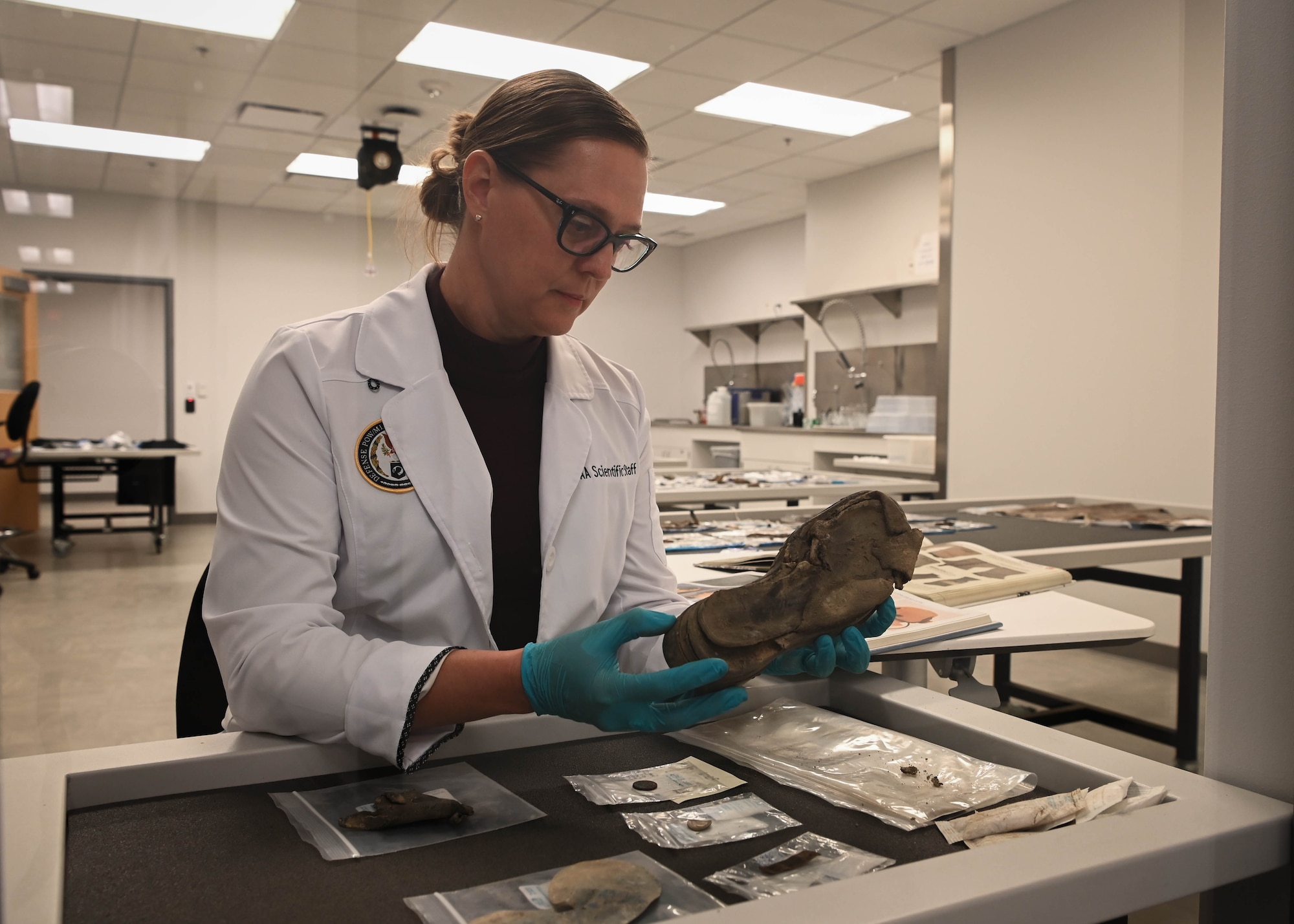 Dr. Traci Van Deest, Defense POW/MIA Accounting Agency forensic anthropologist, examines material evidence from World War II at the DPAA facility on Offutt Air Force Base, Neb., Sept. 16, 2025. Material evidence is examined to establish conflict era and provide contextual clues to help identify a fallen service member, and their possible rank and unit. (U.S. Air Force photo by Daniel Martinez)