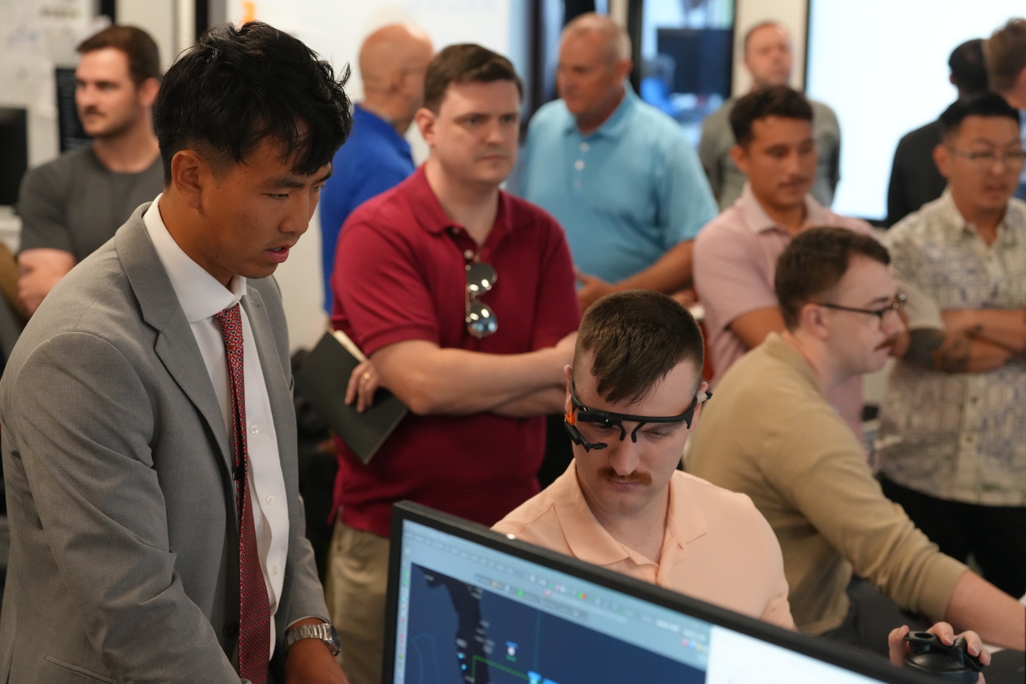 eople sitting in chairs and standing look at computer screens