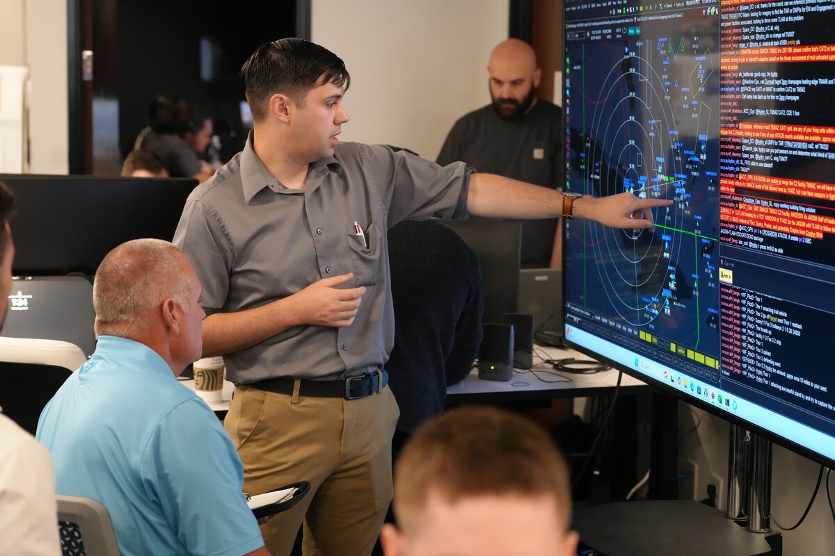people sitting in chairs and listen to ta person standing, pointing at a  large computer screen.