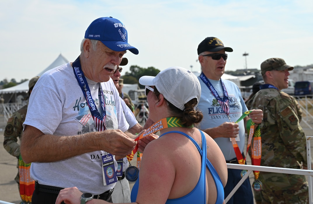 U.S. Air Force Vietnam veteran Bob Lively, left, dons a finishers medal during the Air Force Marathon at Wright-Patterson Air Force Base, Ohio, Sept. 20, 2025. As part of Operation Honor 2025, veterans were on hand to cheer on runners and present medals to winners while also engaging with younger generations of service members before tomorrow's historic Honor Flight on an Air Force Reserve C-17 Globemaster III assigned to the 445th Airlift Wing. (U.S. Air Force photo by Staff Sgt. Johnathan Quiñones)