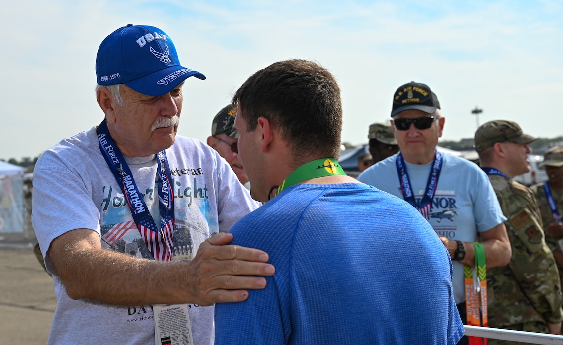 U.S. Air Force Vietnam veteran Bob Lively, left, congratulates an Air Force Marathon runner after donning a finishers medal at Wright-Patterson Air Force Base, Ohio, Sept. 20, 2025. As part of Operation Honor 2025, veterans were on hand to cheer on runners and present medals to winners while also engaging with younger generations of service members before tomorrow's historic Honor Flight on an Air Force Reserve C-17 Globemaster III assigned to the 445th Airlift Wing. (U.S. Air Force photo by Staff Sgt. Johnathan Quiñones)