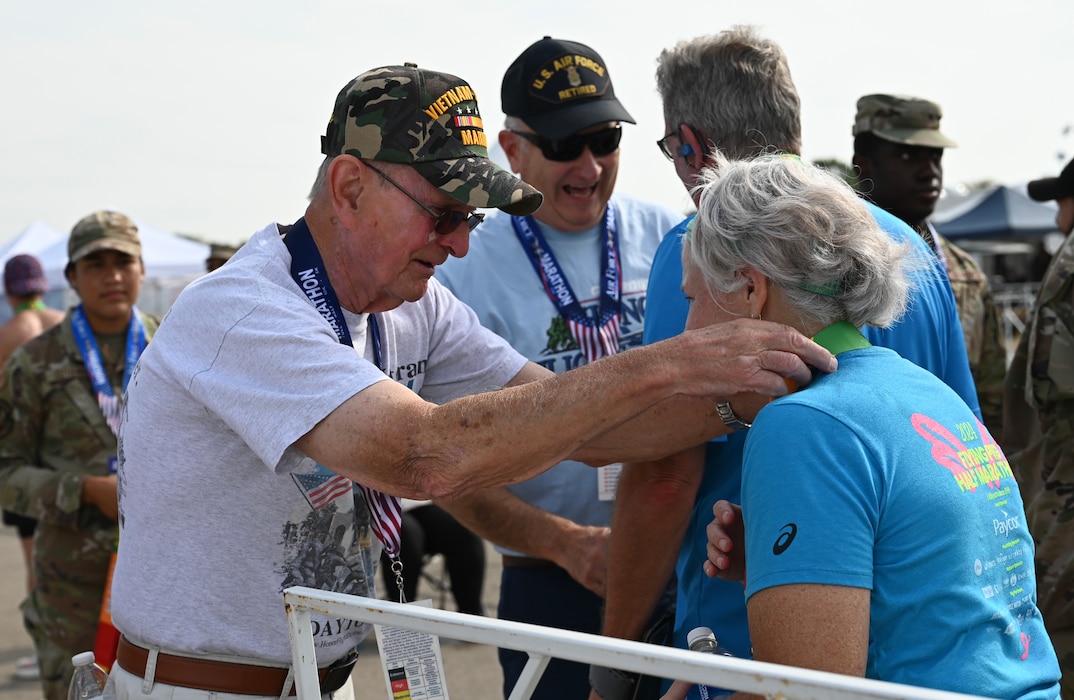 U.S. Marine Vietnam veteran Jim Smith, left, dons a finishers medal during the Air Force Marathon at Wright-Patterson Air Force Base, Ohio, Sept. 20, 2025. As part of Operation Honor 2025, veterans were on hand to cheer on runners and present medals to winners while also engaging with younger generations of service members before tomorrow's historic Honor Flight on an Air Force Reserve C-17 Globemaster III assigned to the 445th Airlift Wing. (U.S. Air Force photo by Staff Sgt. Johnathan Quiñones)