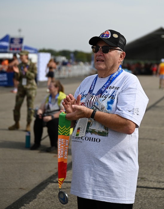 Vietnam veteran Bob Downey cheers for runners in the Air Force Marathon at Wright-Patterson Air Force Base, Ohio, Sept. 20, 2025. As part of Operation Honor 2025, veterans were on hand to cheer on runners and present medals to winners while also engaging with younger generations of service members before tomorrow's historic Honor Flight on an Air Force Reserve C-17 Globemaster III assigned to the 445th Airlift Wing. (U.S. Air Force photo by Staff Sgt. Johnathan Quiñones)
