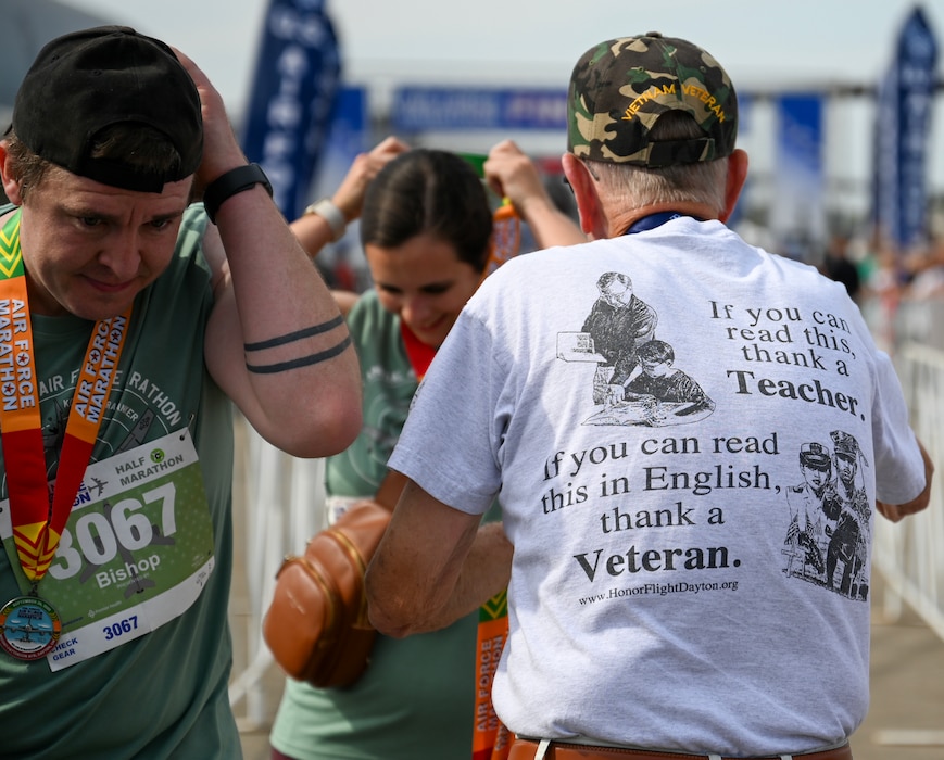 U.S. Marine Corps Vietnam veteran Jim Smith, right, hands a runner a finishers medal at the Air Force Marathon at Wright-Patterson Air Force Base, Ohio, Sept. 20, 2025. As part of Operation Honor 2025, veterans were on hand to cheer on runners and present medals to winners while also engaging with younger generations of service members before tomorrow's historic Honor Flight on an Air Force Reserve C-17 Globemaster III assigned to the 445th Airlift Wing. (U.S. Air Force photo by Staff Sgt. Johnathan Quiñones)