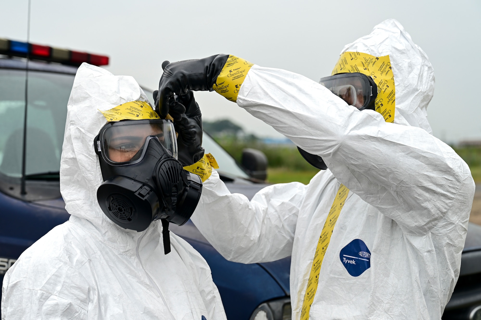 A man applies tape to a womans gas mask.