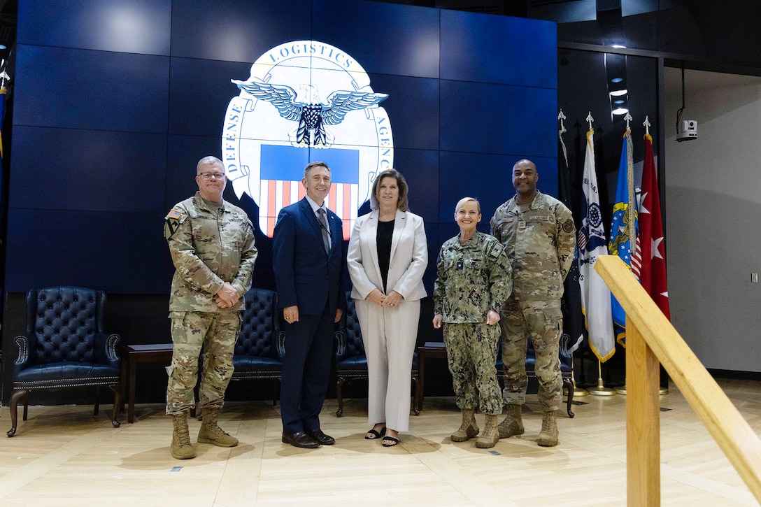 Several people are smiling for the camera on stage. The one in the center was just coined by the DLA Director who is the first one pictured.