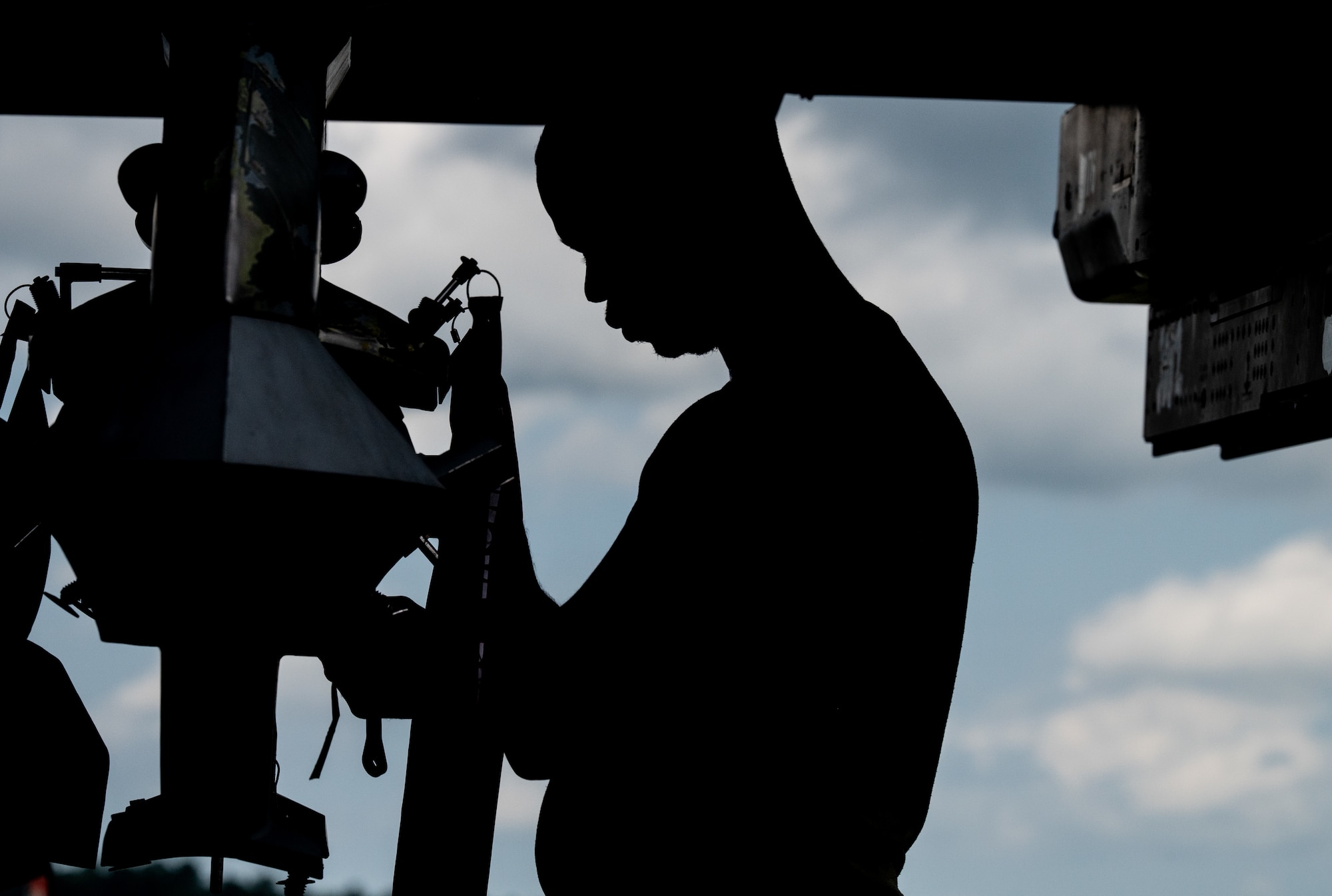 A man in silhouette making adjustments to a jet's missile rail