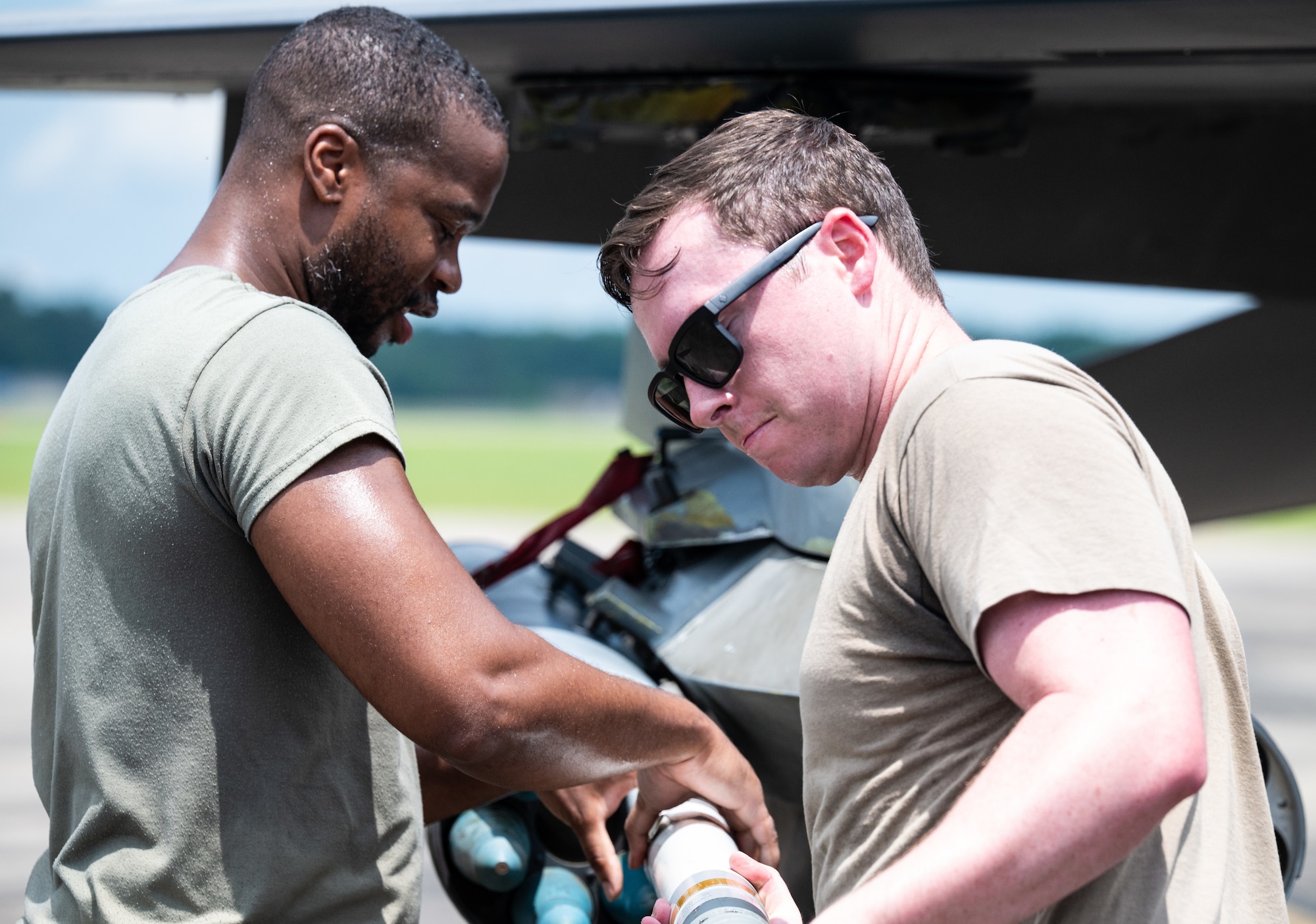 Two male maintainers load a rocket into a rocket launcher on a jet