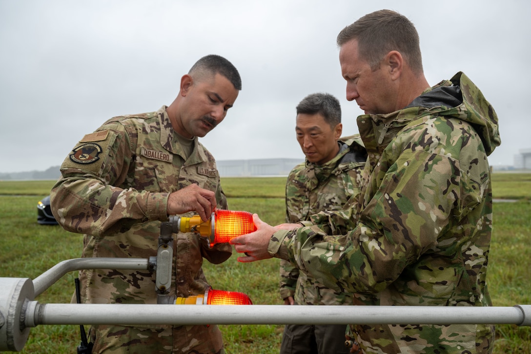 U.S. Air Force Senior Airman Andrew Caballero, 316th Operations Support Squadron radar, airfield and weather systems journeyman, Col. Jun S. Oh, 316th Wing and installation commander, and Chief Master Sgt. Kevin Helms, 316th Wing command chief, screw on the lightbulb cover of the wind mass at Joint Base Andrews, Maryland, Sept. 17, 2025. Changing the light bulb is vital to keeping equipment safe for air traffic controllers supporting military and civilian aircraft in all weather conditions.
