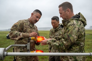 U.S. Air Force Senior Airman Andrew Caballero, 316th Operations Support Squadron radar, airfield and weather systems journeyman, Col. Jun S. Oh, 316th Wing and installation commander, and Chief Master Sgt. Kevin Helms, 316th Wing command chief, screw on the lightbulb cover of the wind mass at Joint Base Andrews, Maryland, Sept. 17, 2025. Changing the light bulb is vital to keeping equipment safe for air traffic controllers supporting military and civilian aircraft in all weather conditions.