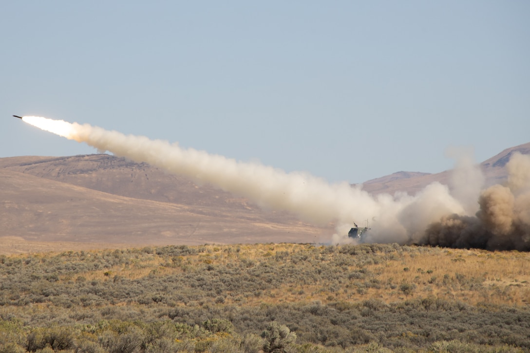 A missile leaves a trail of fiery smoke behind as it launches from a military vehicle parked in a field during the day.