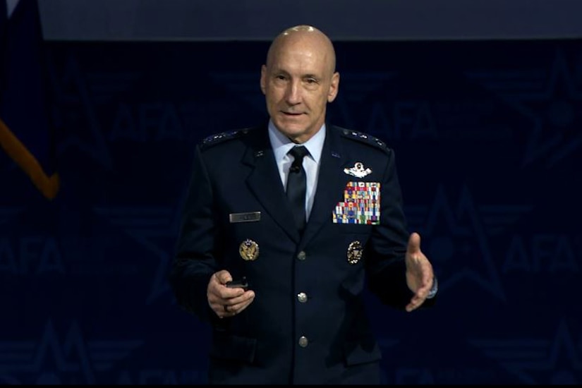 A person in a dress military uniform speaks and gestures with his hands indoors.