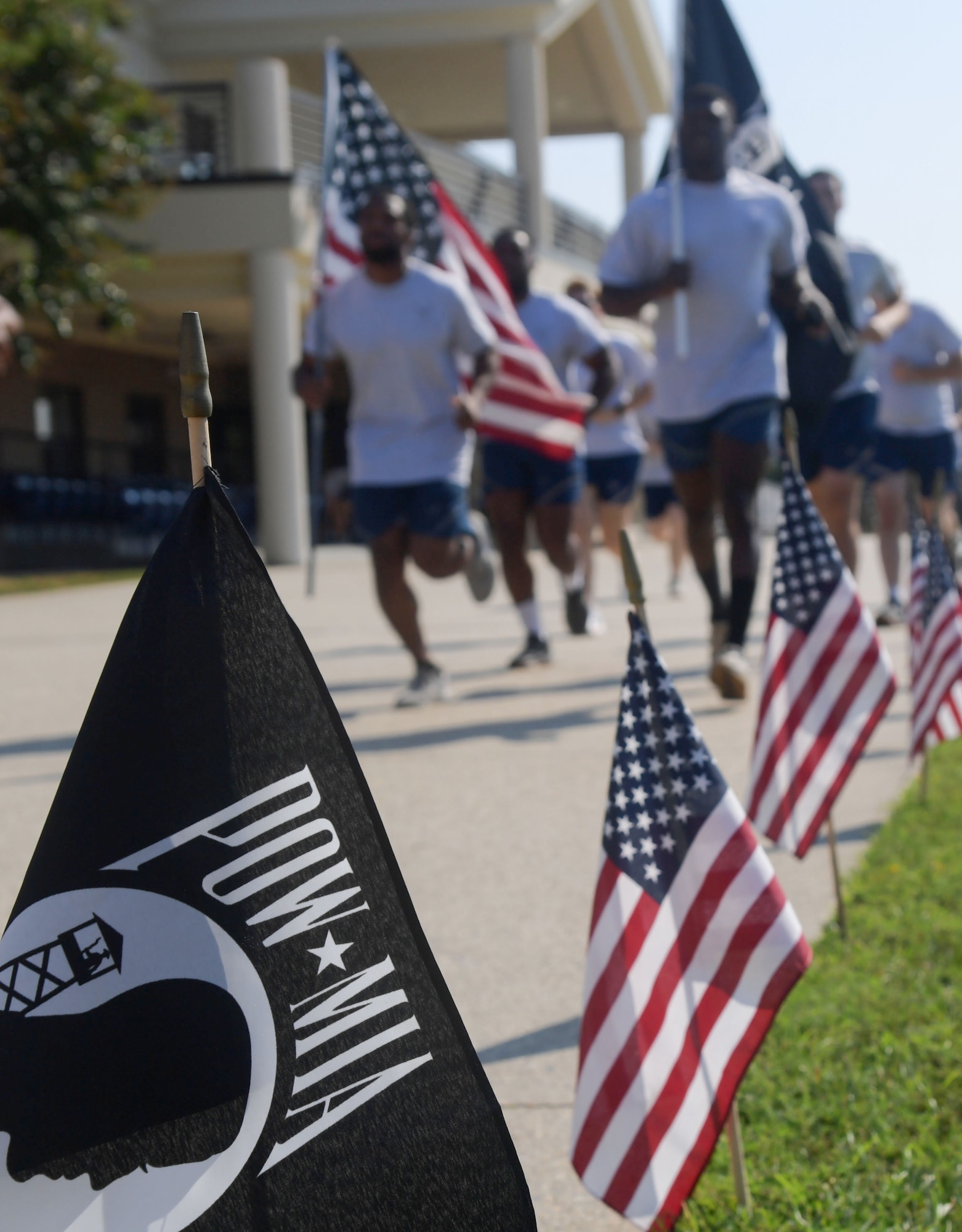 A POW/MIA flag is displayed, while group of people run in the foreground