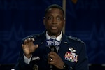 A man seated in a dress uniform speaks into a microphone and gestures.