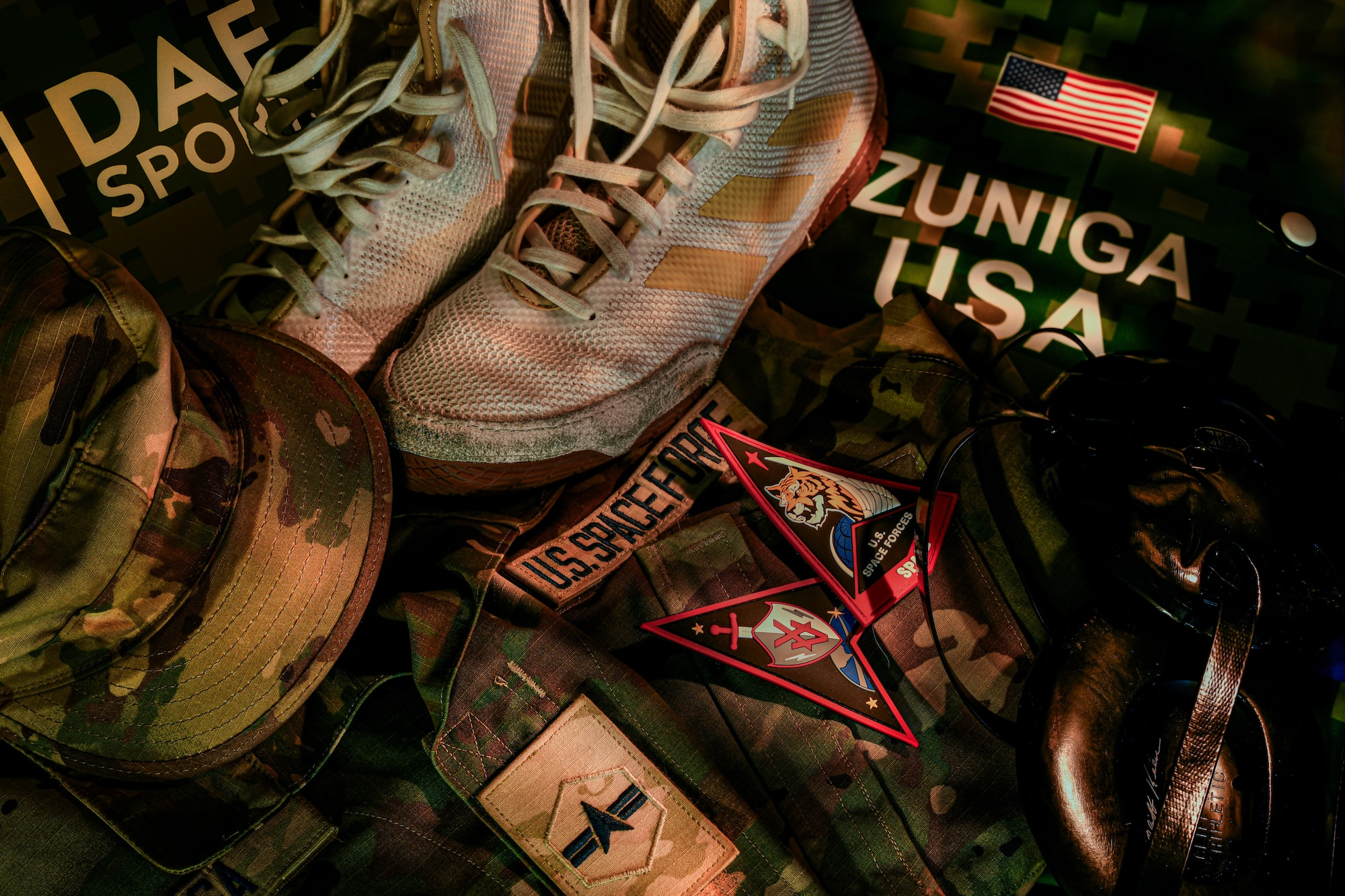 A military cover, blouse and unit patches lay alongside shoes, ear protection and a wrestling singlet