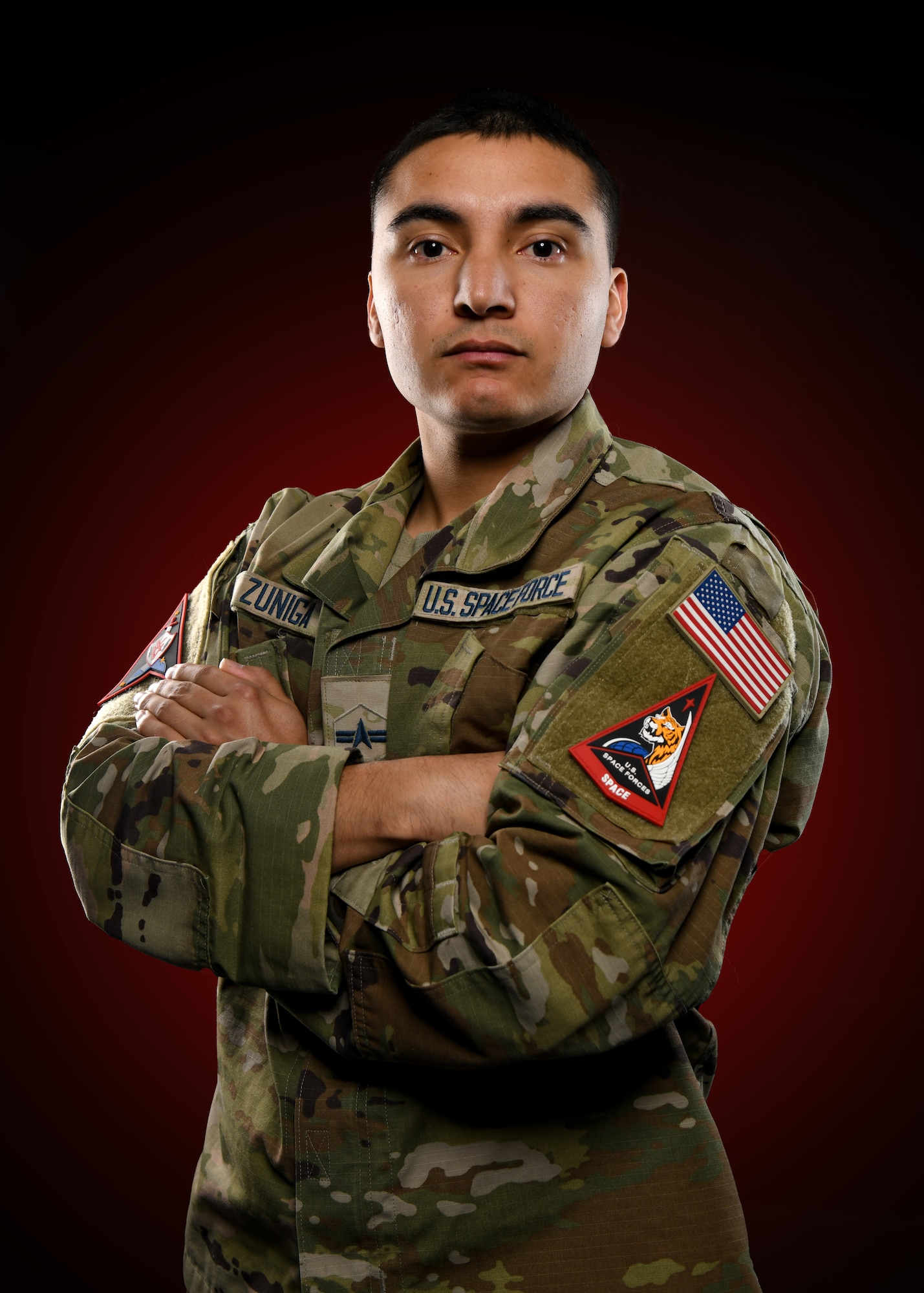 A man in uniform crosses his arms for a medium closeup against a red background