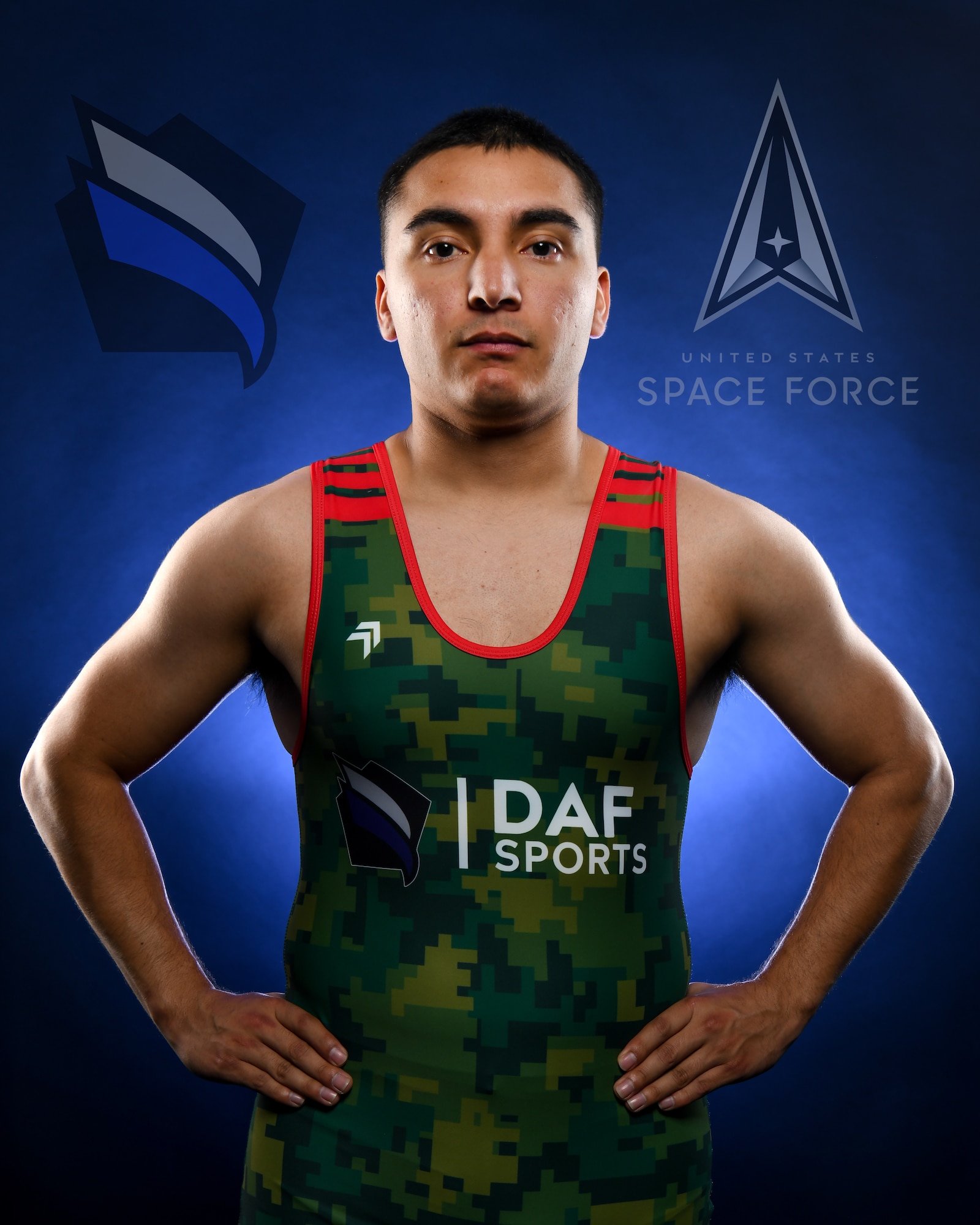 A man in a wrestling singlet poses with his hands on his hips with the DAF Sports and Space Force logos on either side of him