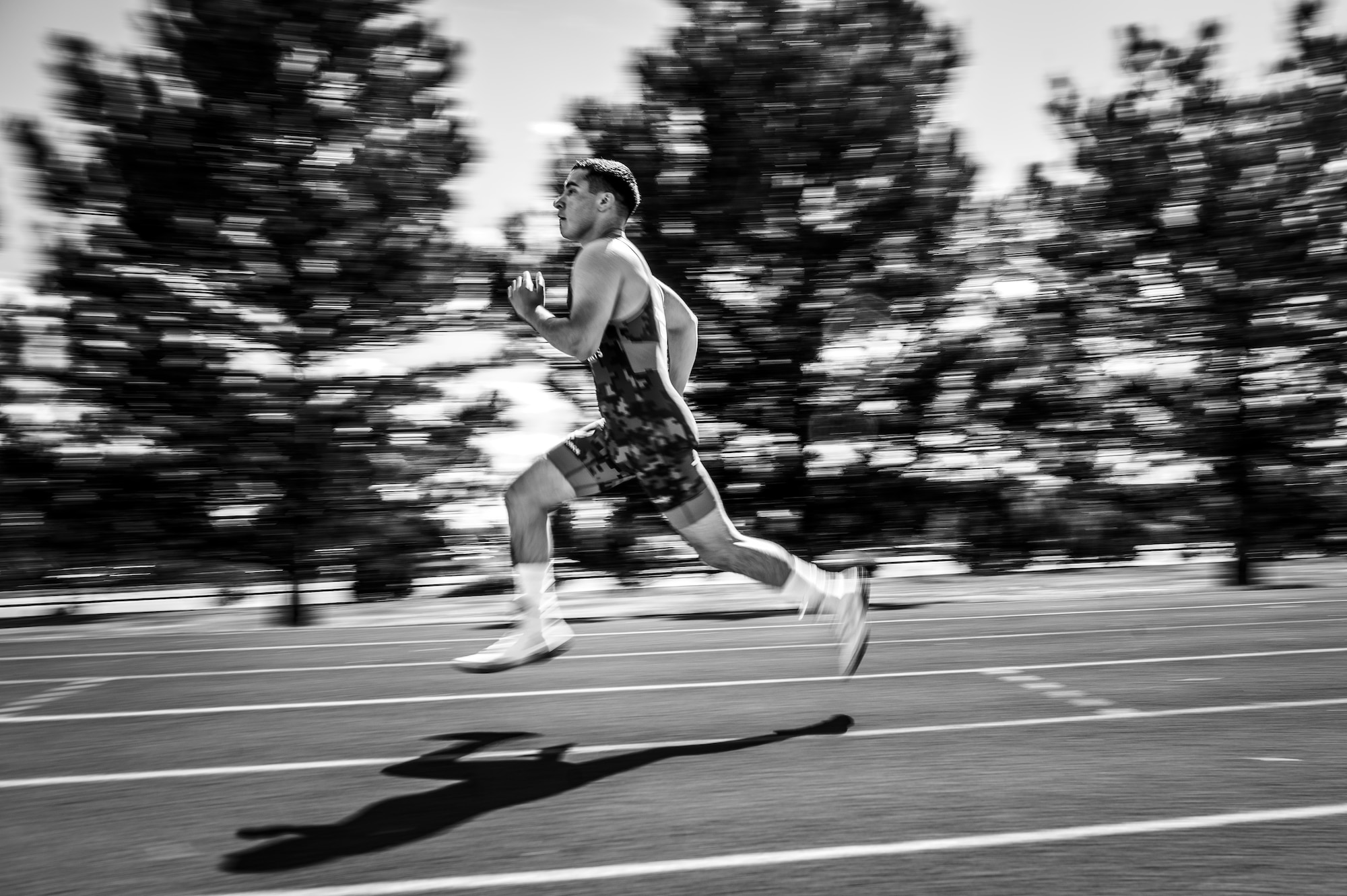 A man in a wrestling singlet is captured in profile running down a track in a black and white photo
