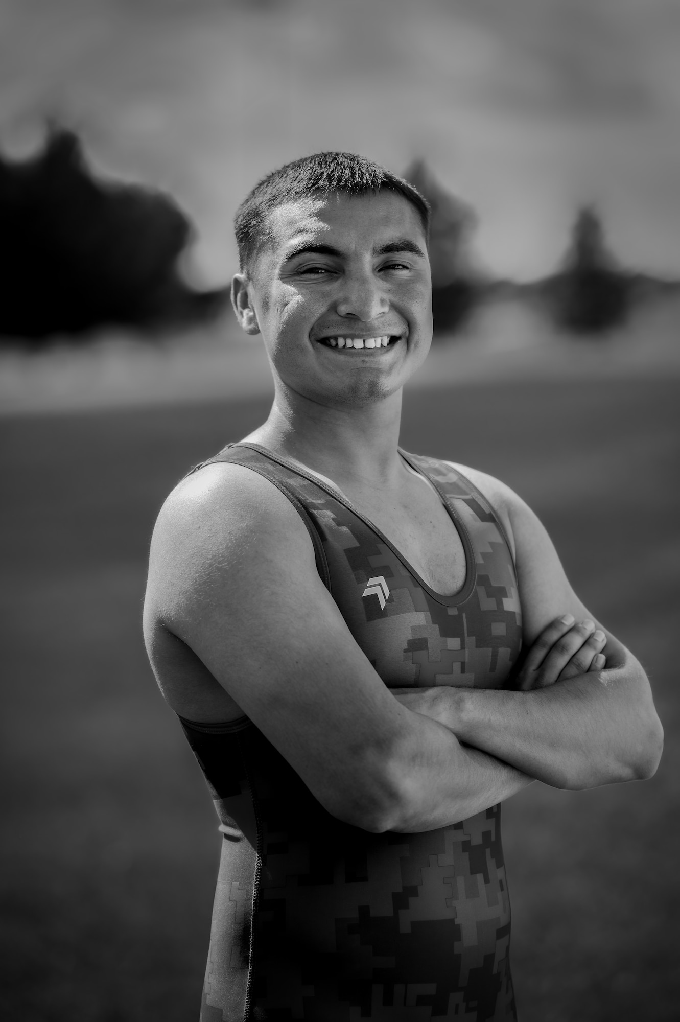 A man in a wrestling singlet poses with his arms crossed, smiling, in a black and white photo