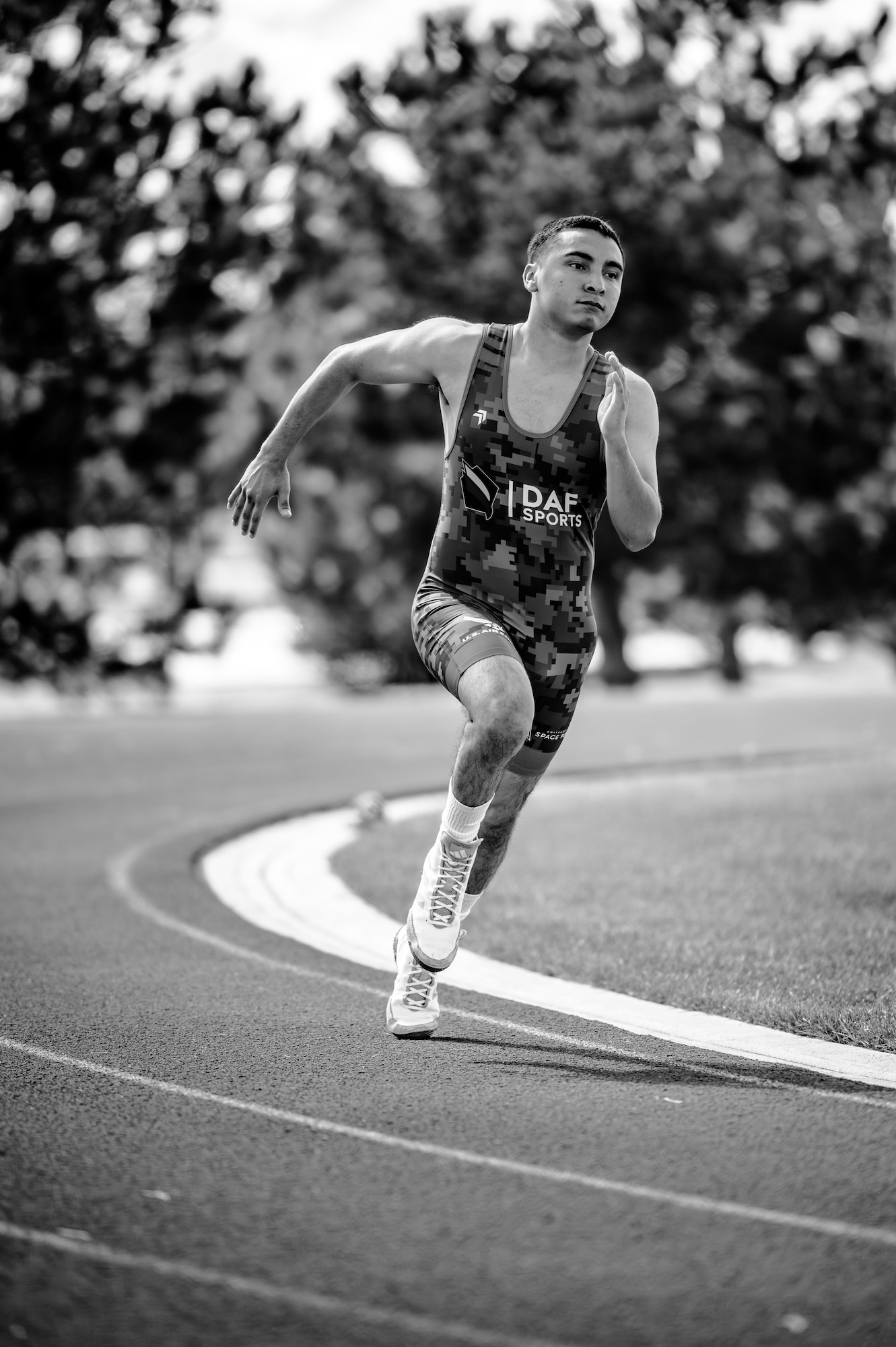 A man in wrestling gear sprints around the bend of a track in a black and white photo