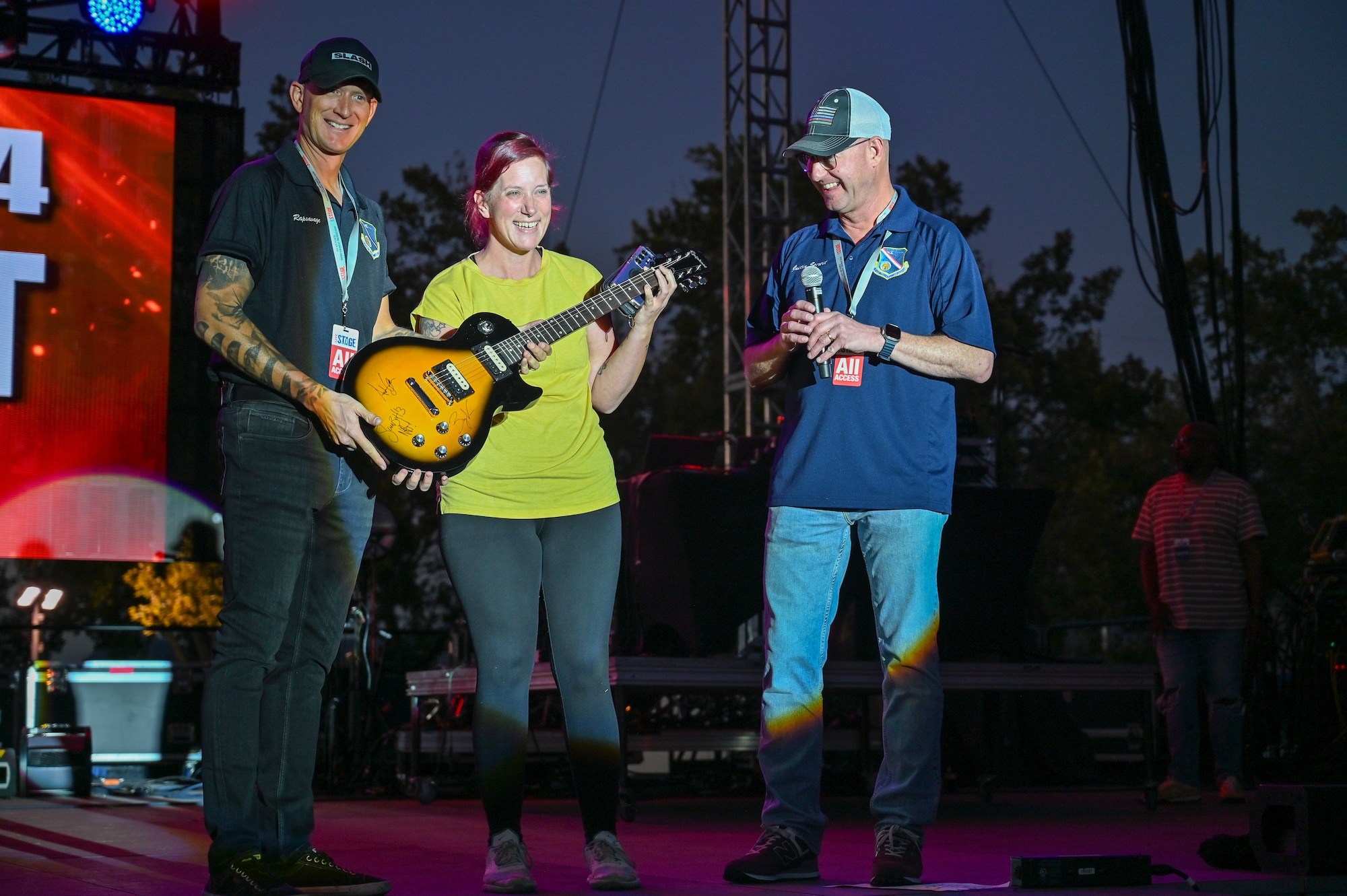 Two people give a guitar to another person on stage