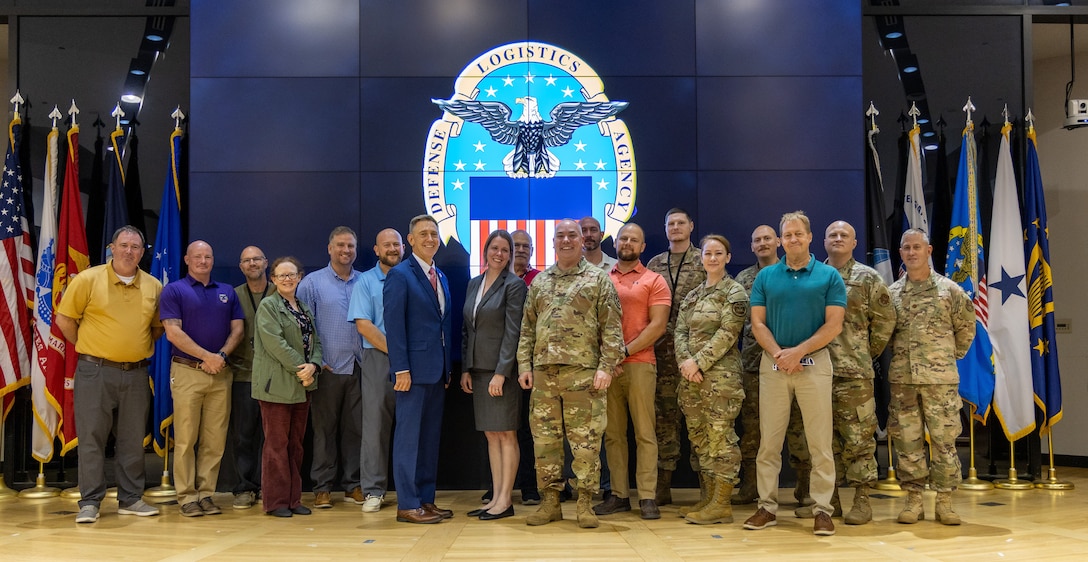 Large group pose for a photo on stage with large screen in background with DLA emblem