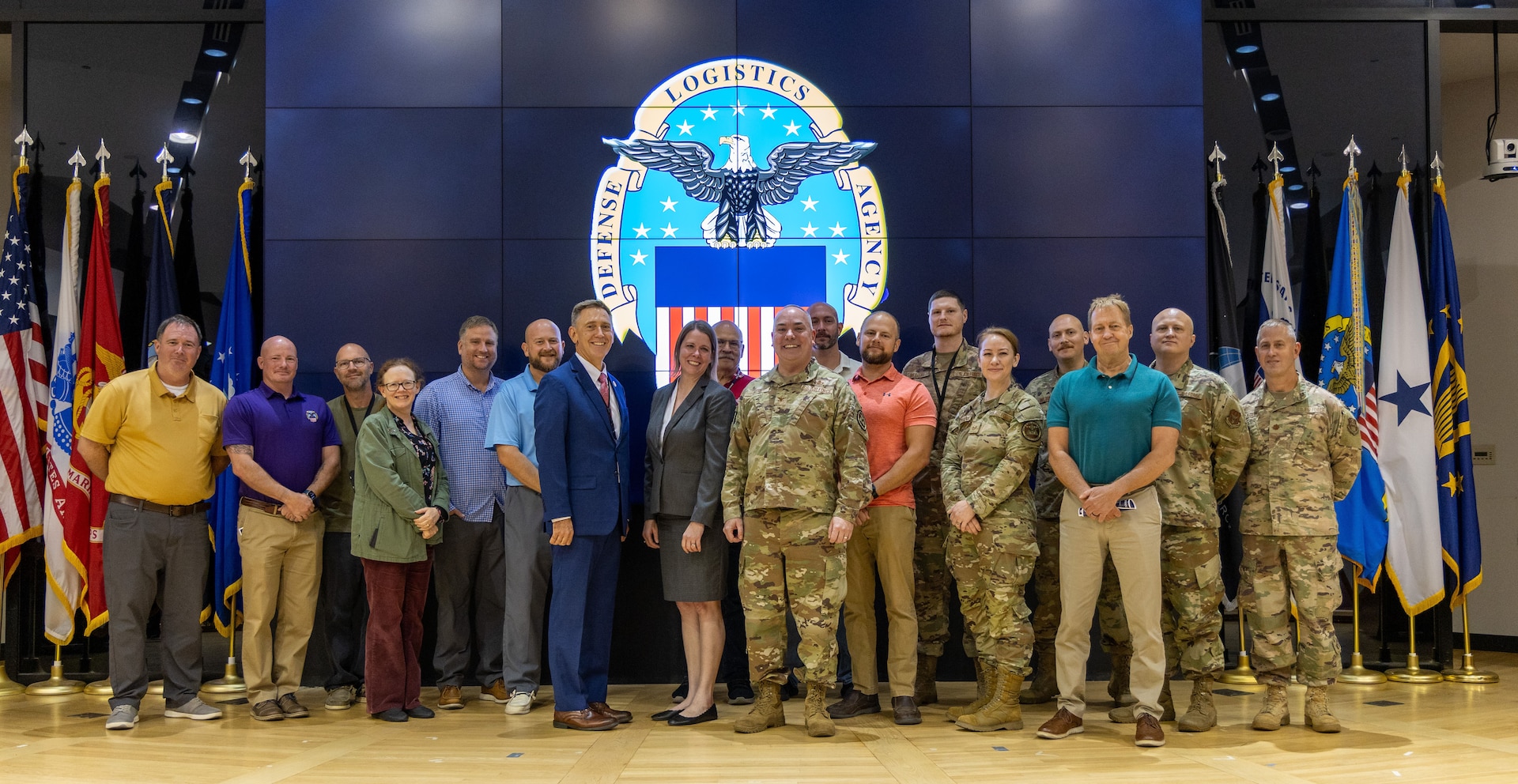 Large group pose for a photo on stage with large screen in background with DLA emblem