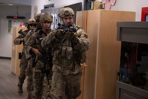 A group of four military members walk in a line holding rifles
